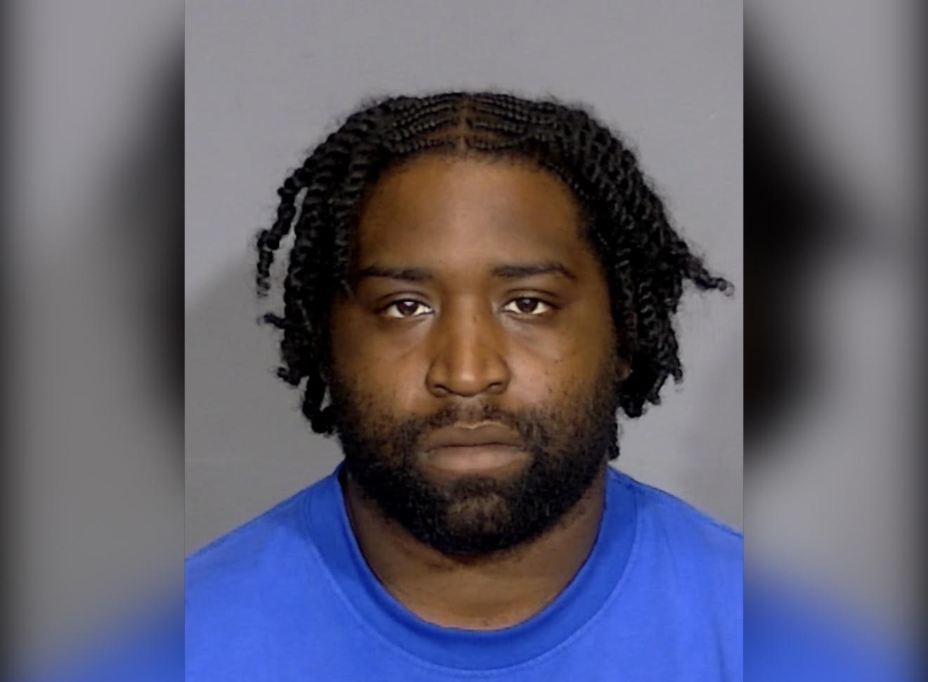 Headshot of a Black man with braided hair and a beard, wearing a blue shirt and looking directly at the camera.