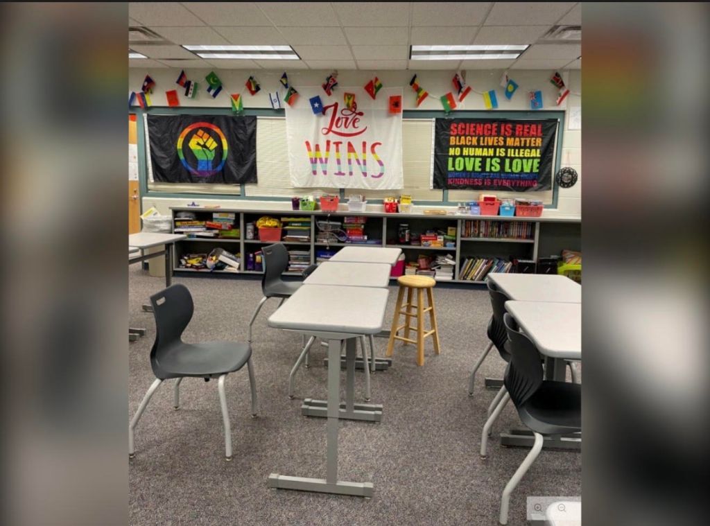 Classroom with diverse decor and signage, including "Love Wins", "Science is real, Black lives matter, no human is illegal, Love is love", and a rainbow flag.