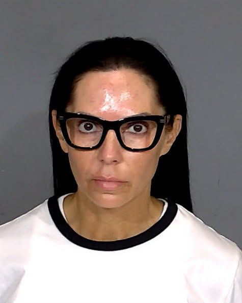 A person wearing glasses and a white shirt, with a serious expression on their face.