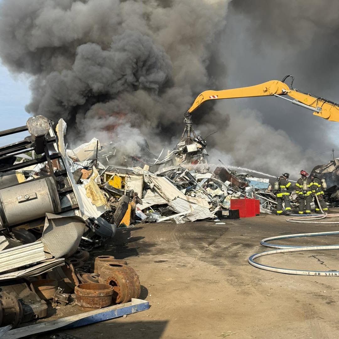 Firefighters and emergency responders at the scene of a large fire, with heavy smoke and debris visible.