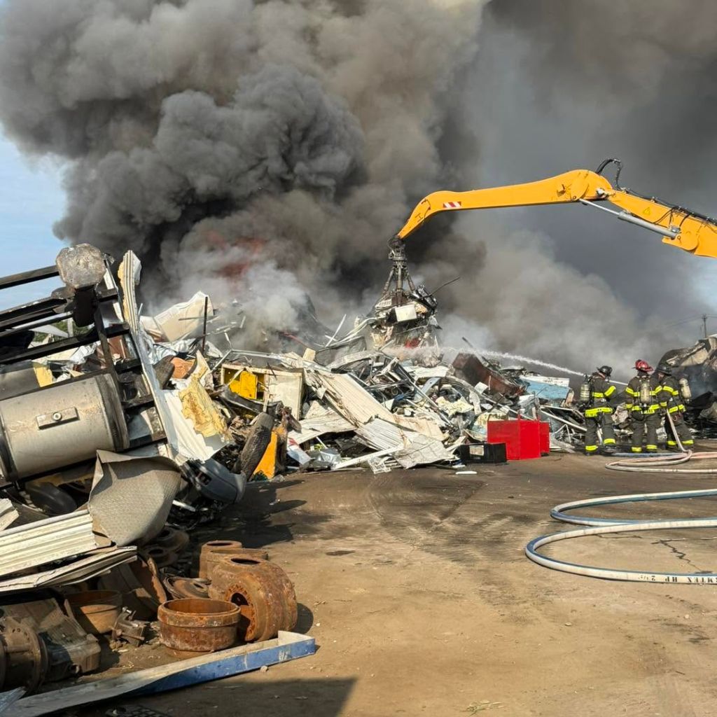Firefighters and emergency responders at the scene of a large fire, with heavy smoke and debris visible.