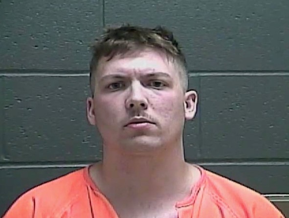 Mugshot of a young man with short hair wearing an orange jumpsuit and looking directly at the camera.