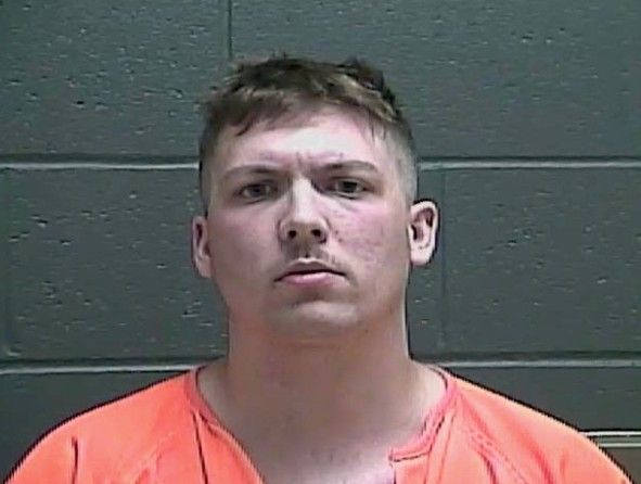 Mugshot of a young man with short hair wearing an orange jumpsuit and looking directly at the camera.