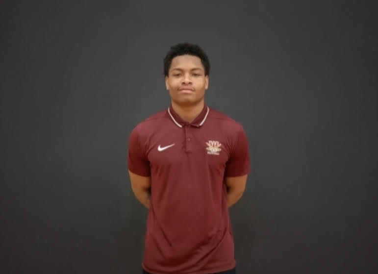 A young man wearing a red Nike polo shirt with the Nike logo visible, standing against a dark background.