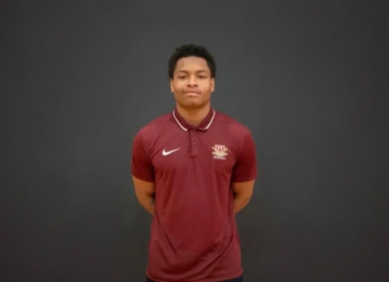 A young man wearing a red Nike polo shirt with the Nike logo visible, standing against a dark background.