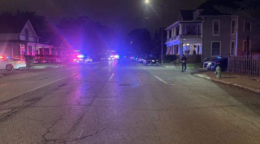 A nighttime street scene with emergency vehicles, their blue and red lights illuminating the buildings and street.