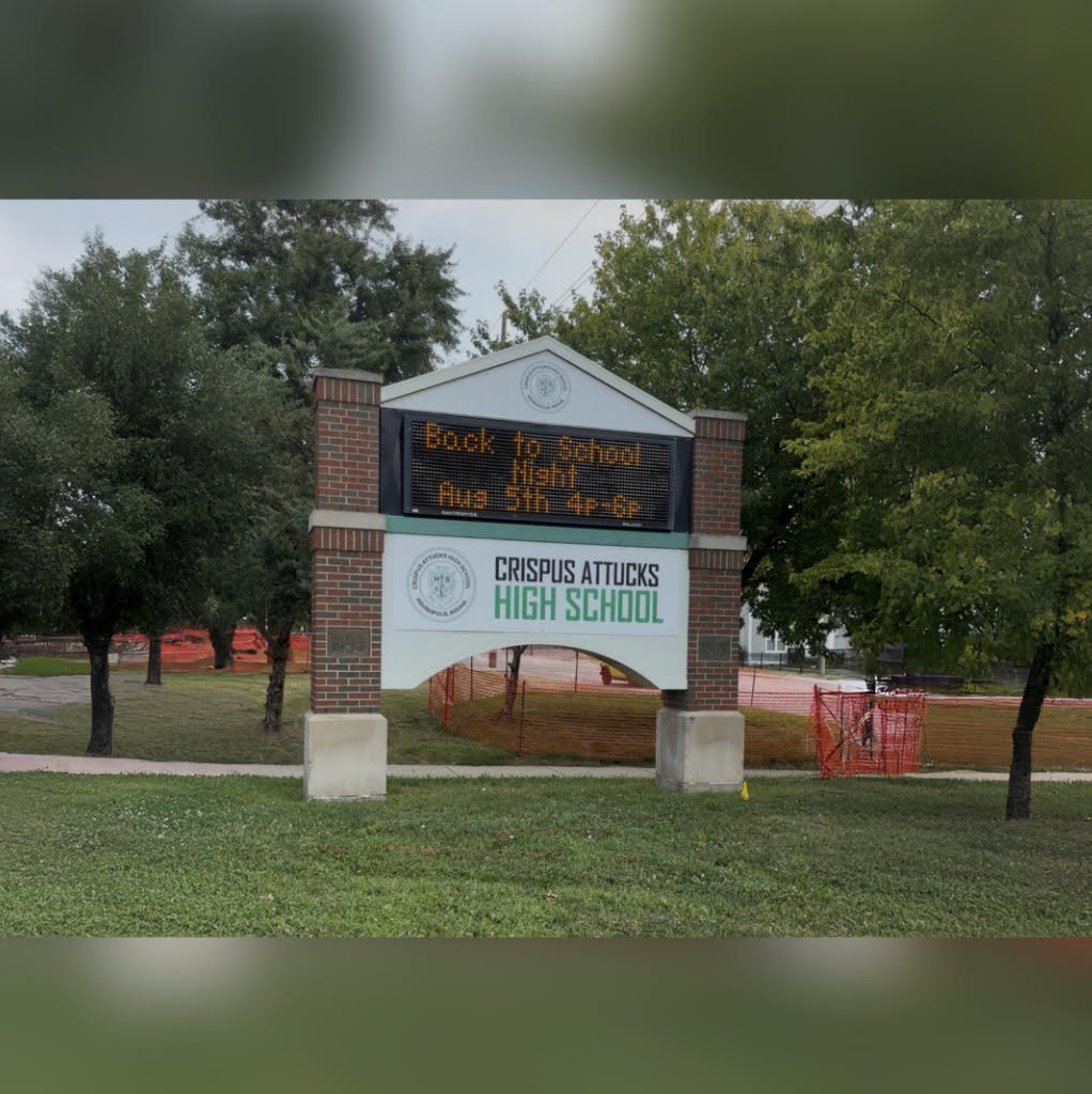 Brick building with sign reading "Crispus Attucks High School". The sign displays the message "Back to school night Aug 5th".