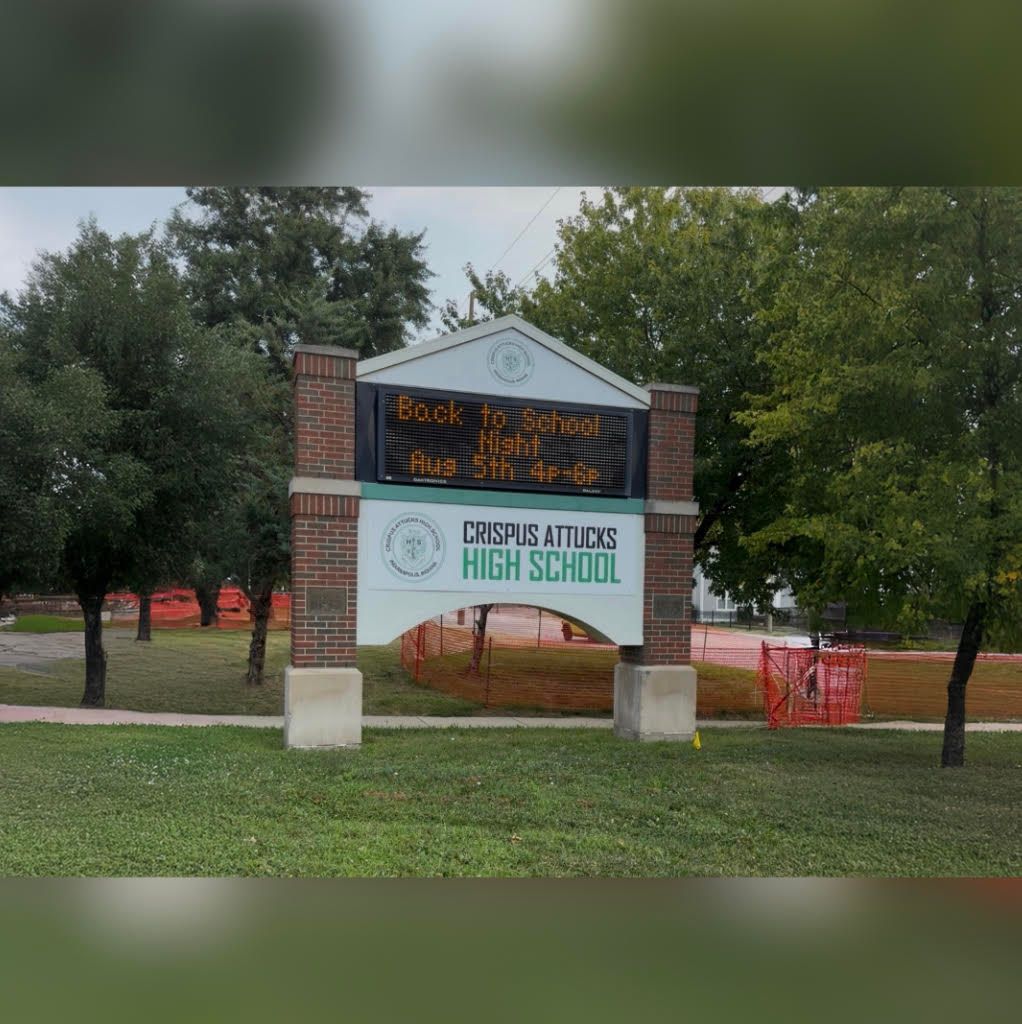 Brick building with sign reading "Crispus Attucks High School". The sign displays the message "Back to school night Aug 5th".
