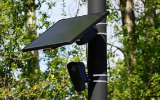 A solar-powered security camera mounted on a pole in a wooded area.