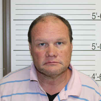 Mugshot of a middle-aged man with a serious expression, wearing a striped shirt against a lineup backdrop with height markings.