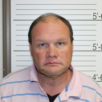 Mugshot of a middle-aged man with a serious expression, wearing a striped shirt against a lineup backdrop with height markings.