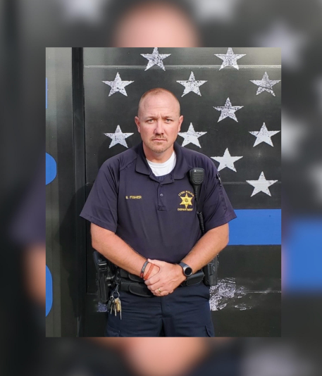 A uniformed police officer standing in front of a backdrop with white stars.