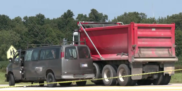 A large red dump truck with a gray cab is parked on the side of the road, surrounded by trees and foliage.