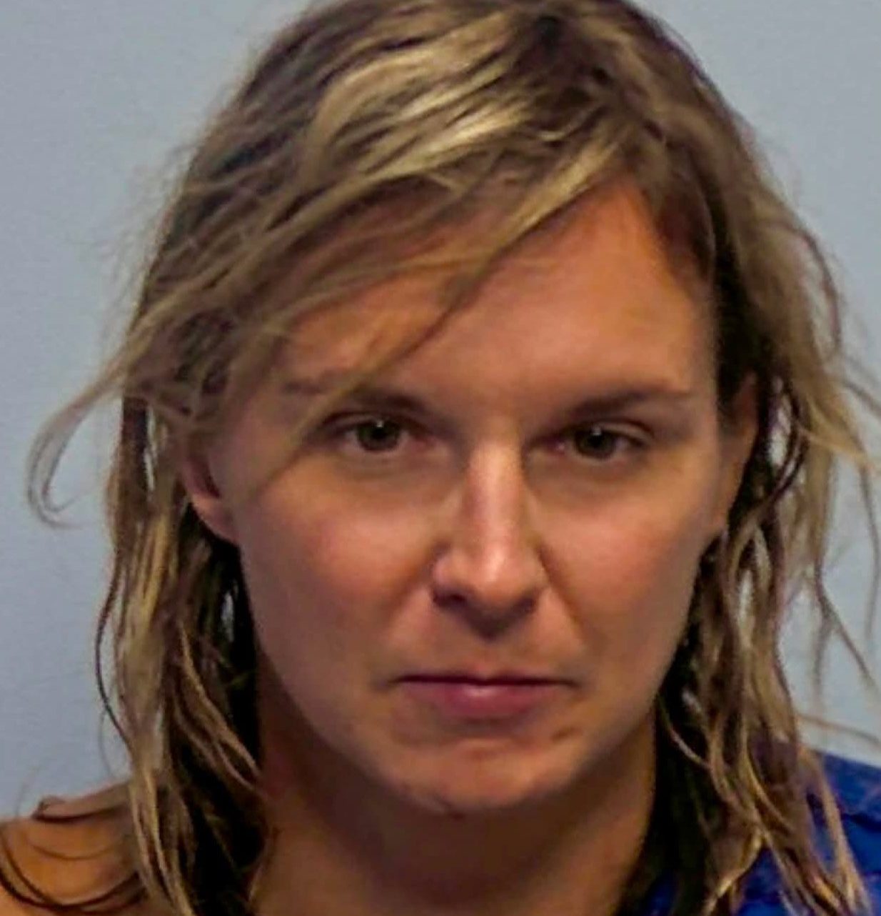 A middle-aged woman with shoulder-length blonde hair and a serious expression, wearing a blue shirt.