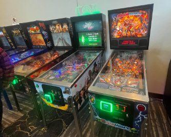 Pinball machines and arcade cabinets in a game room setting, with various colorful and illuminated displays.