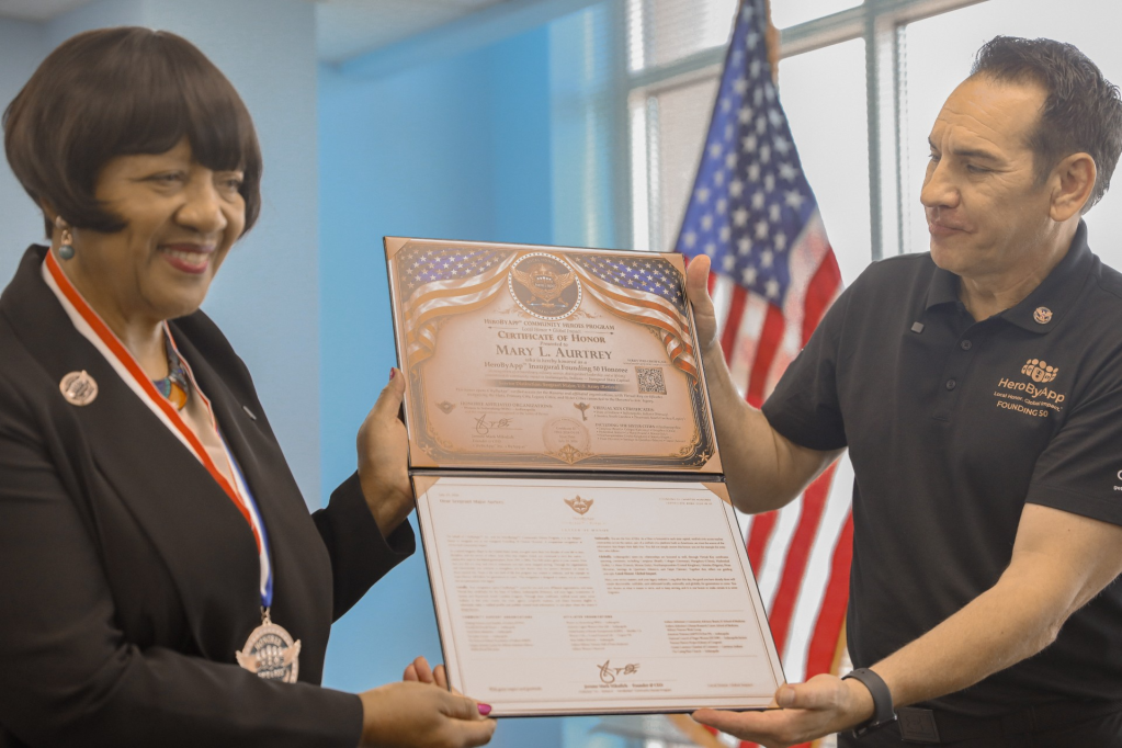 Two people, a woman and a man, standing together and holding a certificate of honor presented to the woman.
