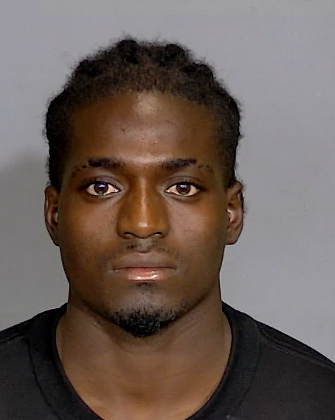 Headshot of a young Black man with short curly hair and a serious expression, wearing a black shirt.