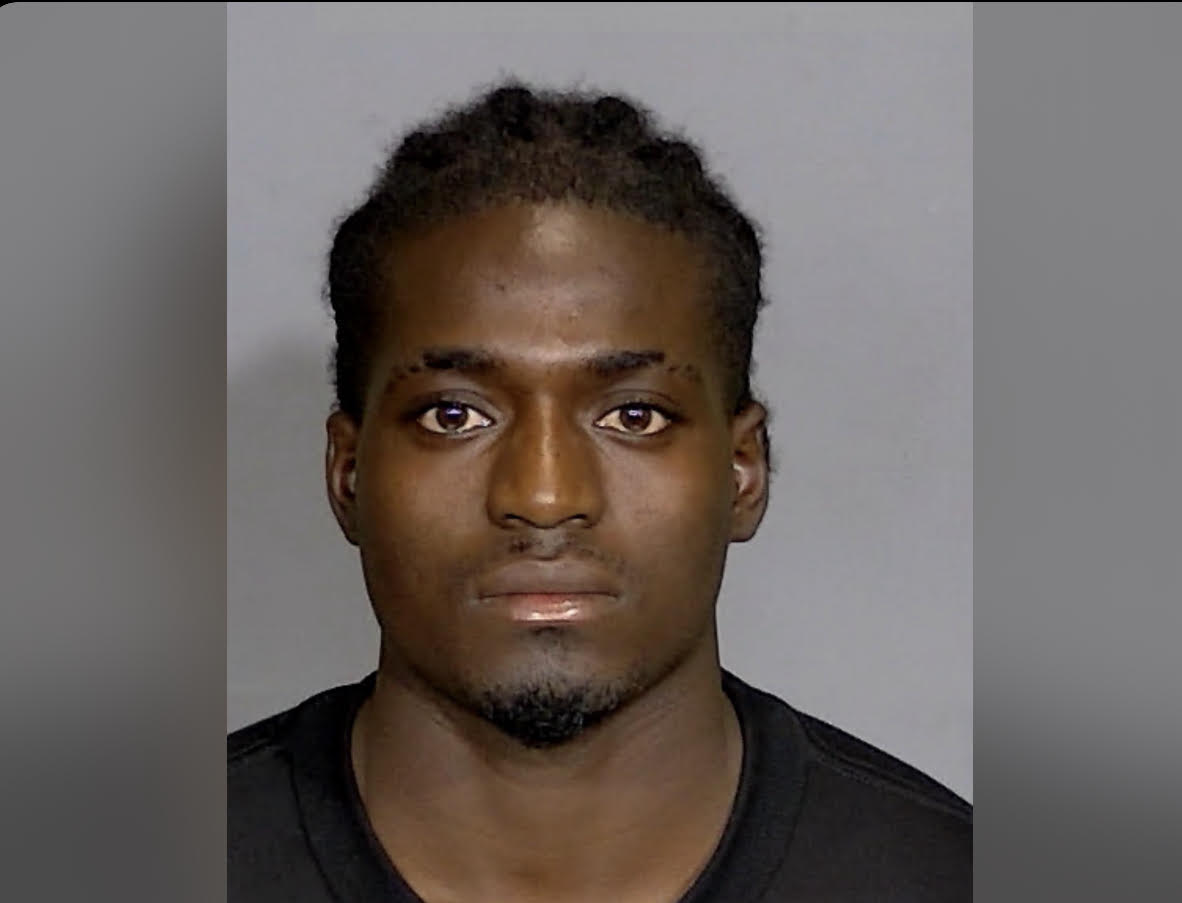 Headshot of a young Black man with a serious expression, wearing a black shirt against a plain background.