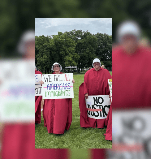 Two people wearing red robes holding signs that say "We are all Americans immigrants" and "No justice".
