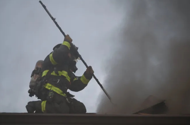 Firefighter in protective gear using a hose to extinguish smoke and flames.