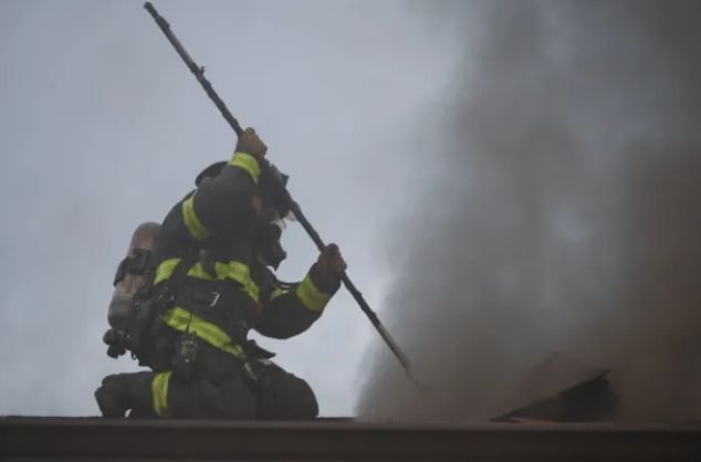 Firefighter in protective gear using a hose to extinguish smoke and flames.