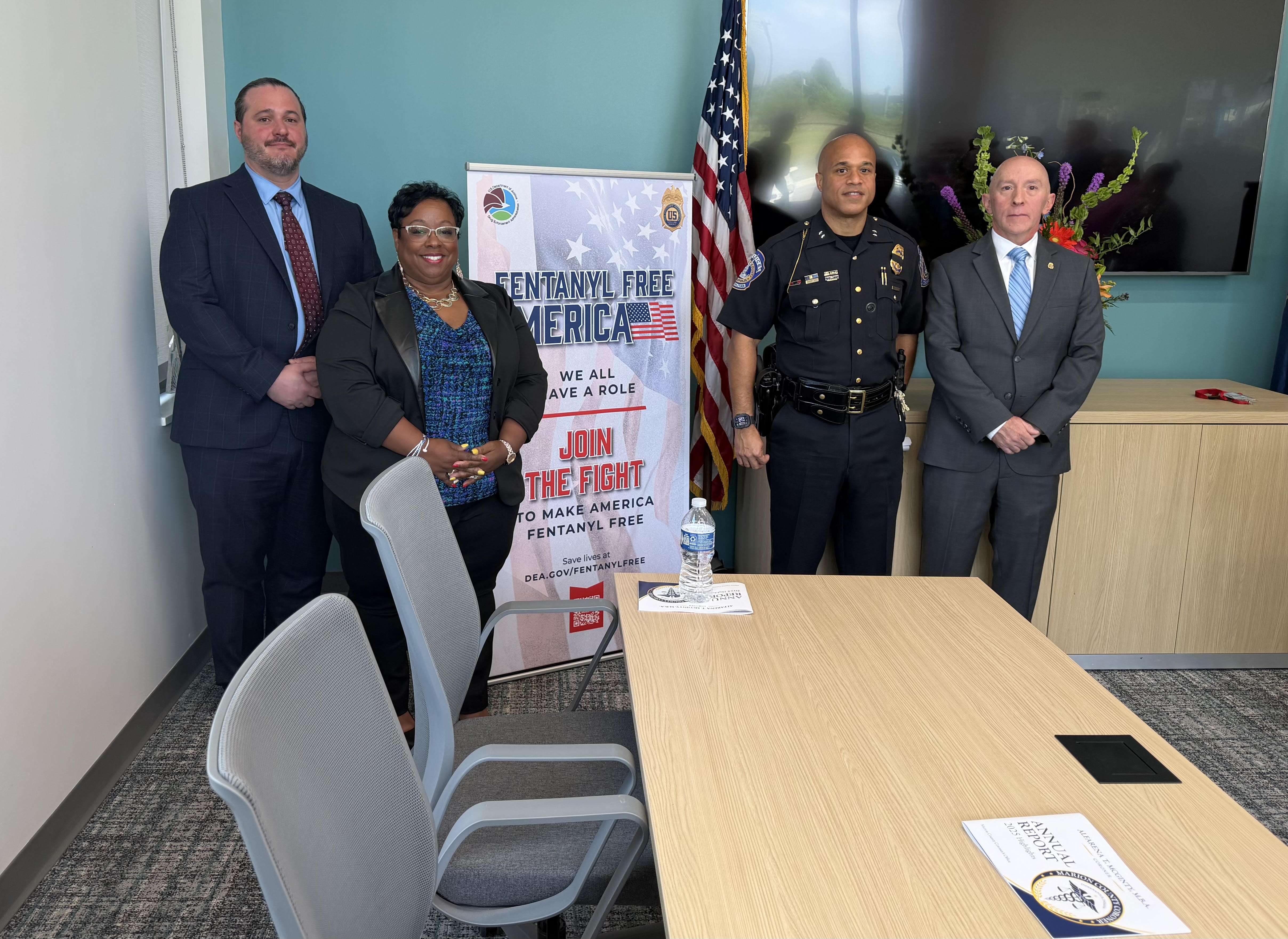 Four people standing in an office, one holding a poster that says "Fentanyl Free America: We All Have a Role. Join the Fight to Make America Fentanyl Free.