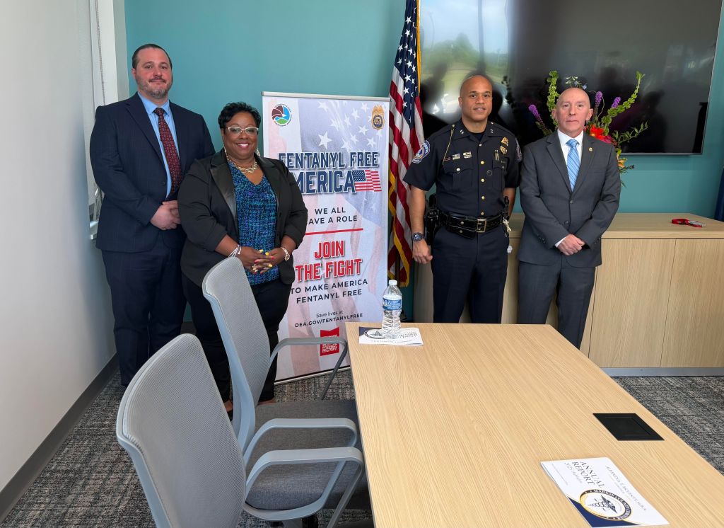 Four people standing in an office, one holding a poster that says "Fentanyl Free America: We All Have a Role. Join the Fight to Make America Fentanyl Free.