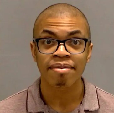 A bald man with glasses wearing a purple shirt and looking directly at the camera.