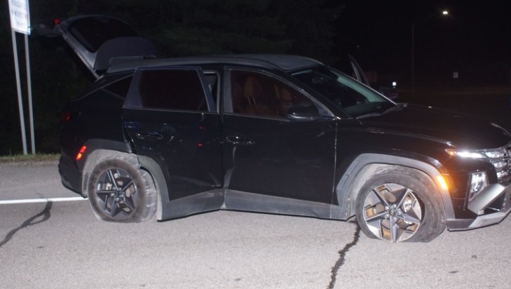 A damaged black SUV with a cracked windshield and damaged front end, parked on a dark street at night.