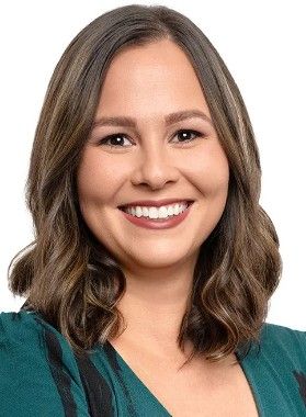 A smiling woman with wavy brown hair wearing a teal blouse.