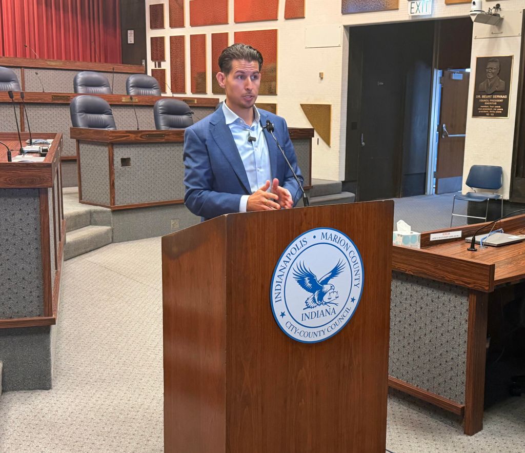 A man in a suit speaking at a podium with the seal of the Indianapolis-Marion County, Indiana government displayed.