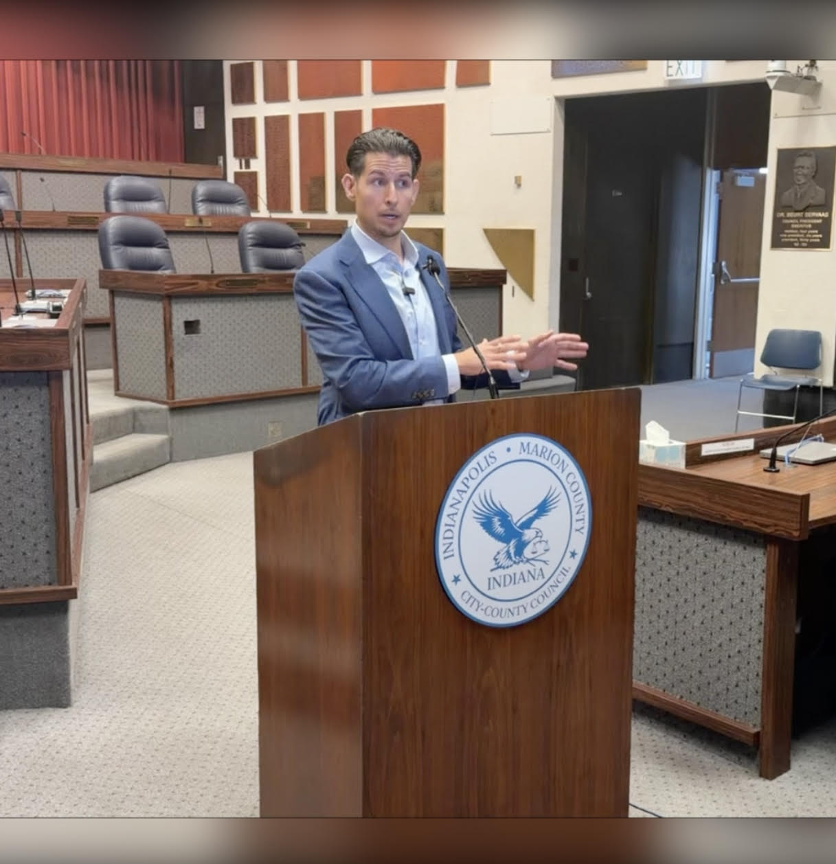 A man in a suit speaking at a podium with the Indianapolis-Marion County logo.