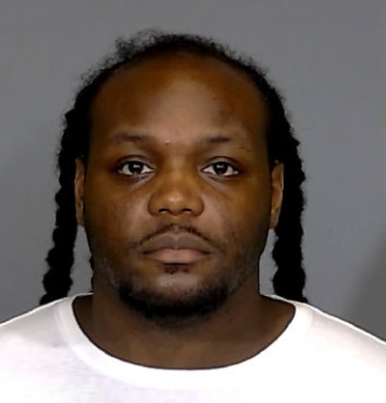 Headshot of a man with dreadlocks wearing a white shirt.
