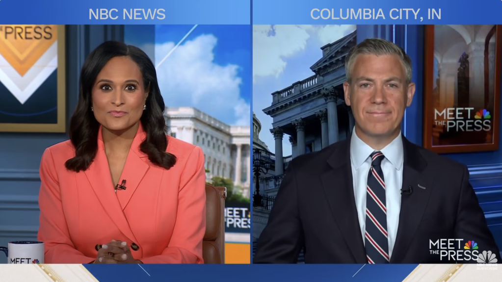 Two news anchors on an NBC News set, one woman in a red jacket and one man in a suit, with a "Meet the Press" backdrop and the Columbia City, IN location displayed.