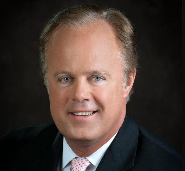 Headshot of a smiling middle-aged man with gray hair wearing a dark suit and red tie.