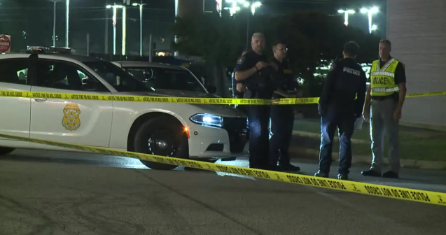 Police officers and emergency personnel at the scene of an incident, with police vehicles and yellow caution tape visible.