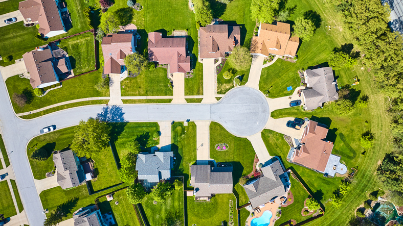 Aerial downward view rooftops suburban homes with green summer lawns