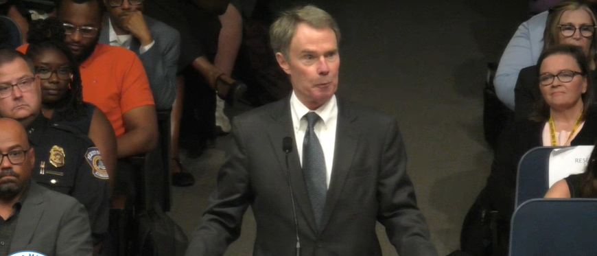 A man in a suit standing in a crowd of people, some wearing uniforms.