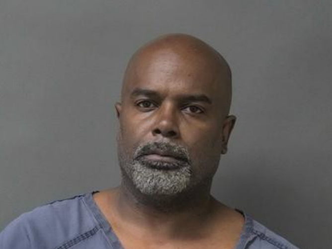 Headshot of a bald, middle-aged Black man with a gray beard, wearing a blue shirt and looking directly at the camera with a serious expression.