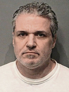 Headshot of a middle-aged man with gray hair and a serious expression, wearing a white shirt.