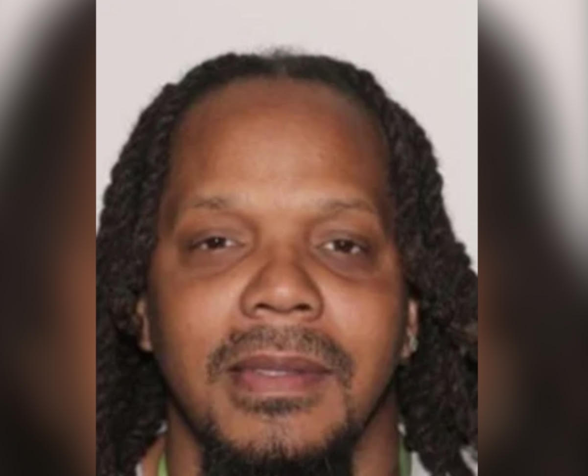 A close-up portrait of a man with dreadlocks and a serious expression.