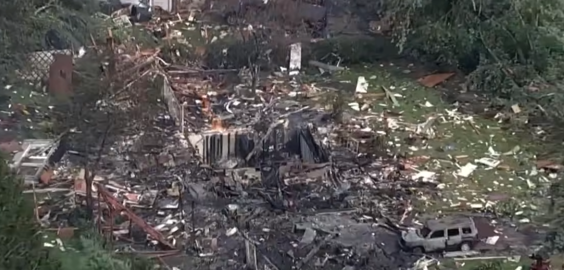 Aerial view of a destroyed residential area with debris, damaged buildings, and a vehicle visible.