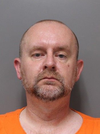 Mugshot of a middle-aged man with a beard, wearing an orange prison uniform.
