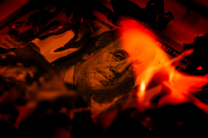 US one hundred dollar bill burning in fire with flames and charred edges close up