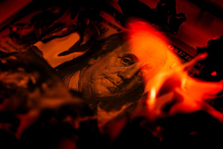 US one hundred dollar bill burning in fire with flames and charred edges close up