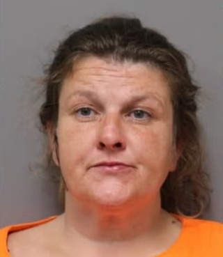 Mugshot of a middle-aged woman with curly brown hair wearing an orange shirt.