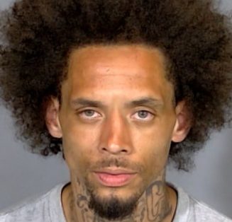 Headshot of a man with curly dark hair and facial tattoos.