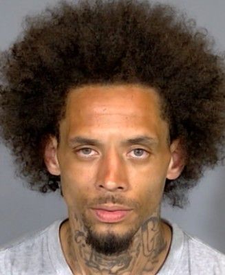 Headshot of a man with curly dark hair and facial tattoos.