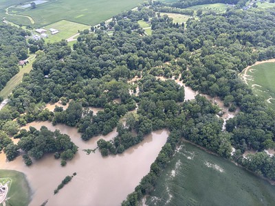 Aerial view of a flooded rural area with a winding river and dense forest.