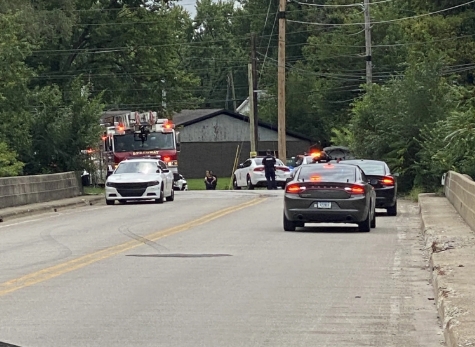 Emergency vehicles and police cars on a road in a wooded area.